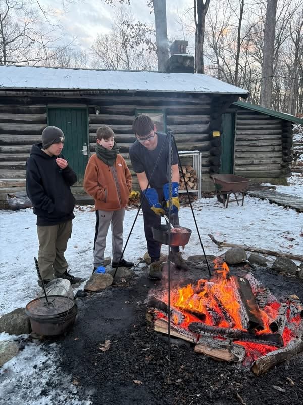 An older Scout teaching younger Scouts to cook over an open fire in winter